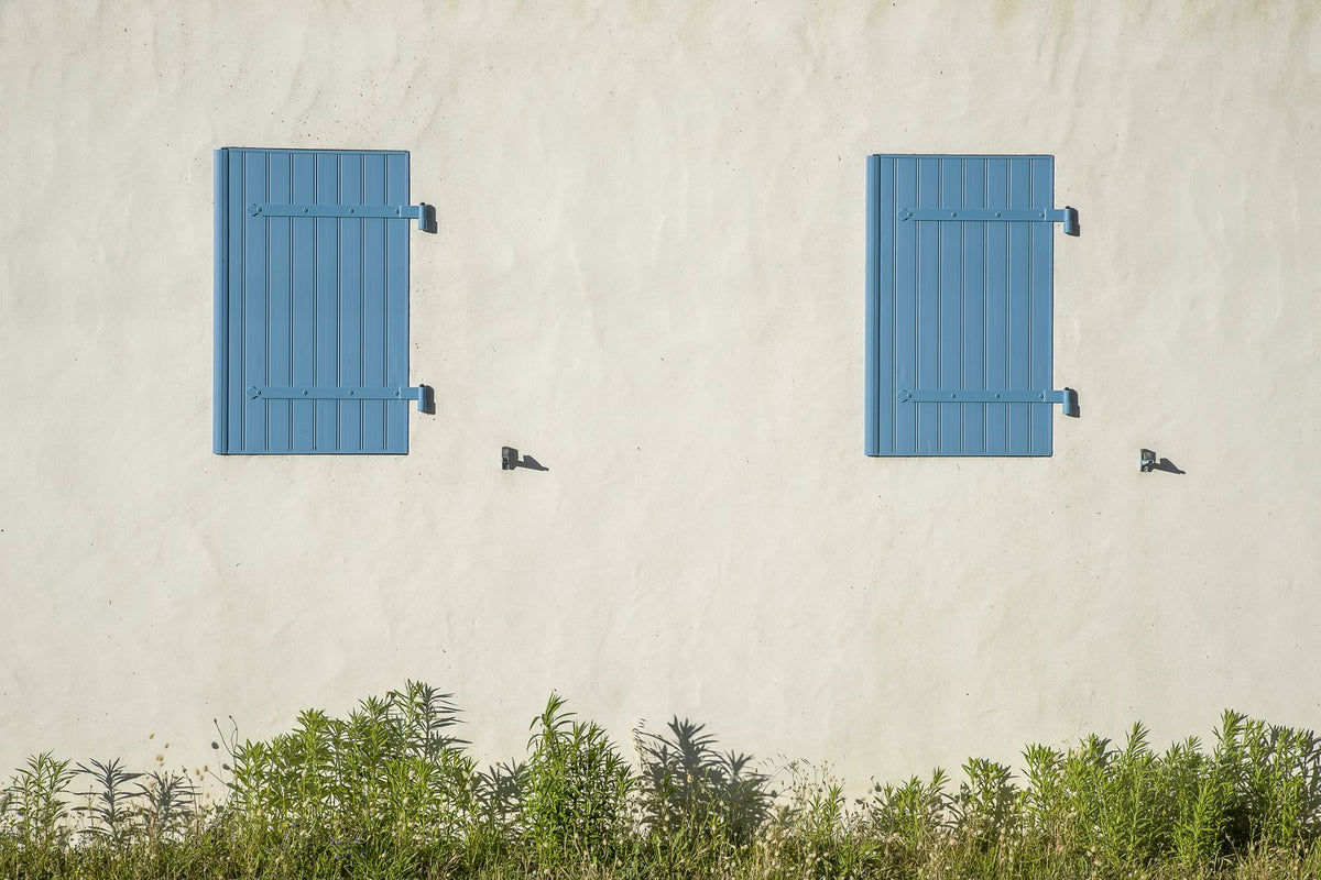 Façade ensoleillée aux volets bleus fermés, décor d'un cadeau pour une maison de vacances rouverte à chaque séjour