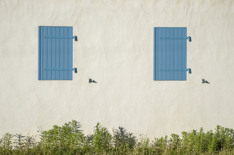 Façade ensoleillée aux volets bleus fermés, décor d'un cadeau pour une maison de vacances rouverte à chaque séjour
